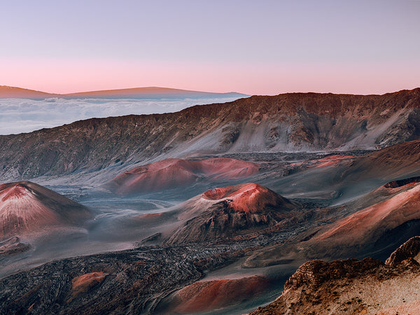 Capture the awe-inspiring volcanic landscape of Haleakalā at sunrise with House of the Sun by Cody Cobb, featuring multi-colored hills and craters beneath a pink and blue sky. Wispy clouds drift in the distance, enhancing Mauis rugged beauty—ideal for elegant framed prints.