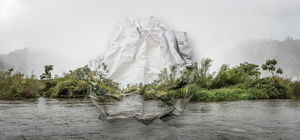 Topographies of Fragility XXV by Ingrid Weyland features a crumpled white paper piece over a lush green river landscape, beautifully blending art with nature by mimicking the surrounding hills and vegetation in a surreal and emotional way.
